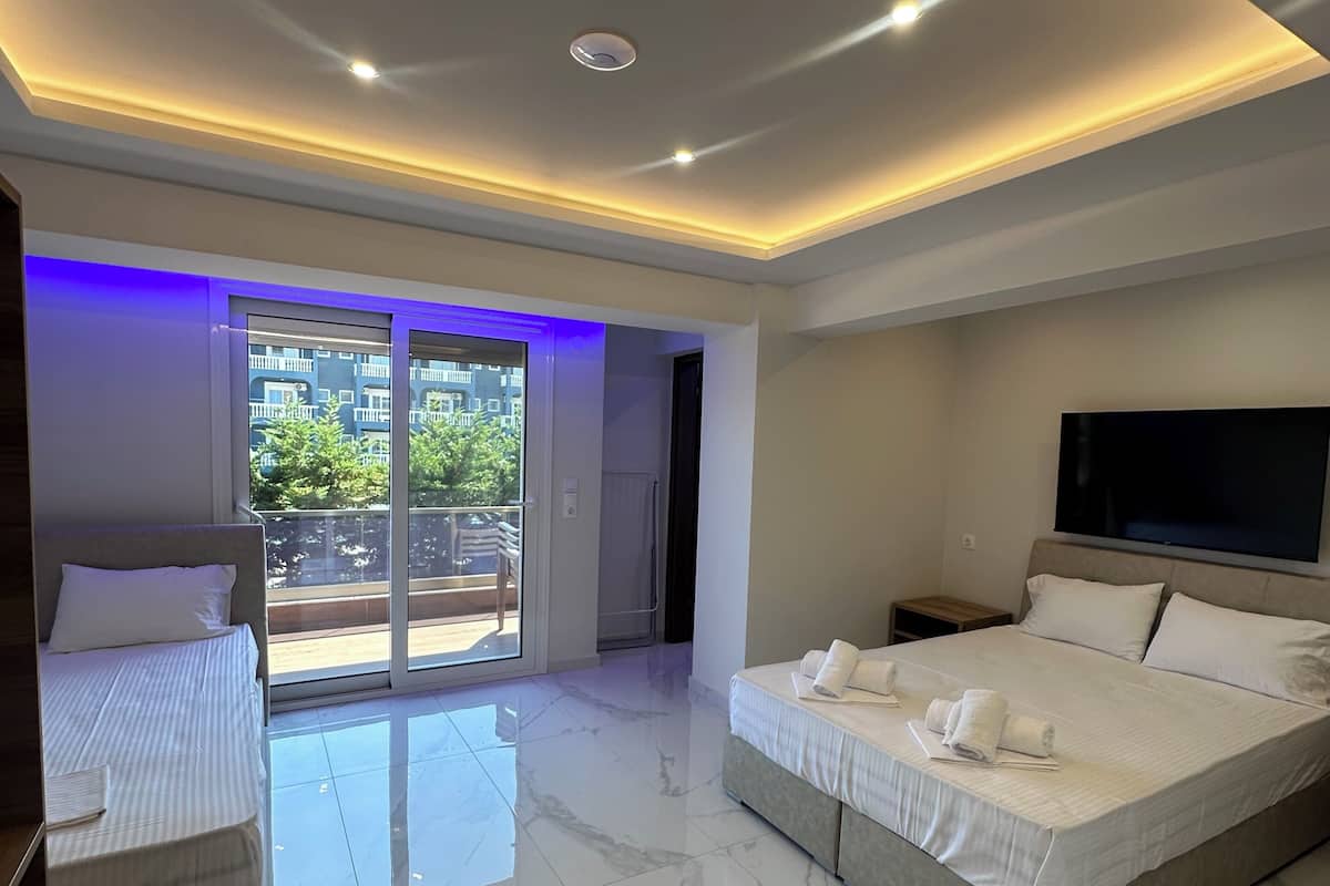 Une chambre moderne avec un grand lit, un plus petit lit, une télévision et un balcon doté de portes vitrées.