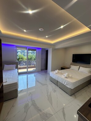 A modern bedroom with a large bed, a smaller bed, a TV, and a balcony with glass doors. - OLYMPIADA GIRNI Suites (Korinos)