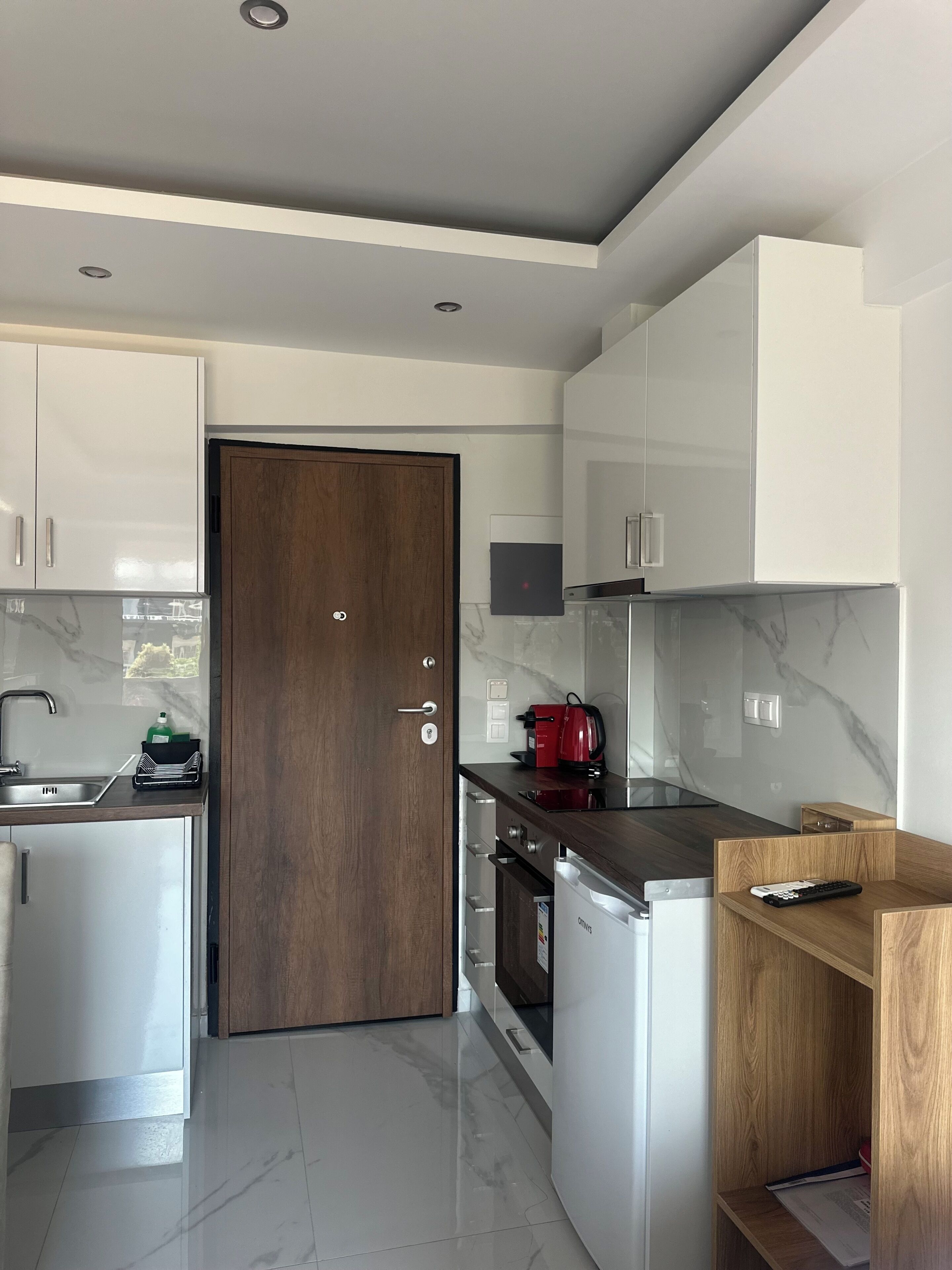 Una cocina moderna con armarios blancos, una puerta de madera, horno empotrado y cafetera.
