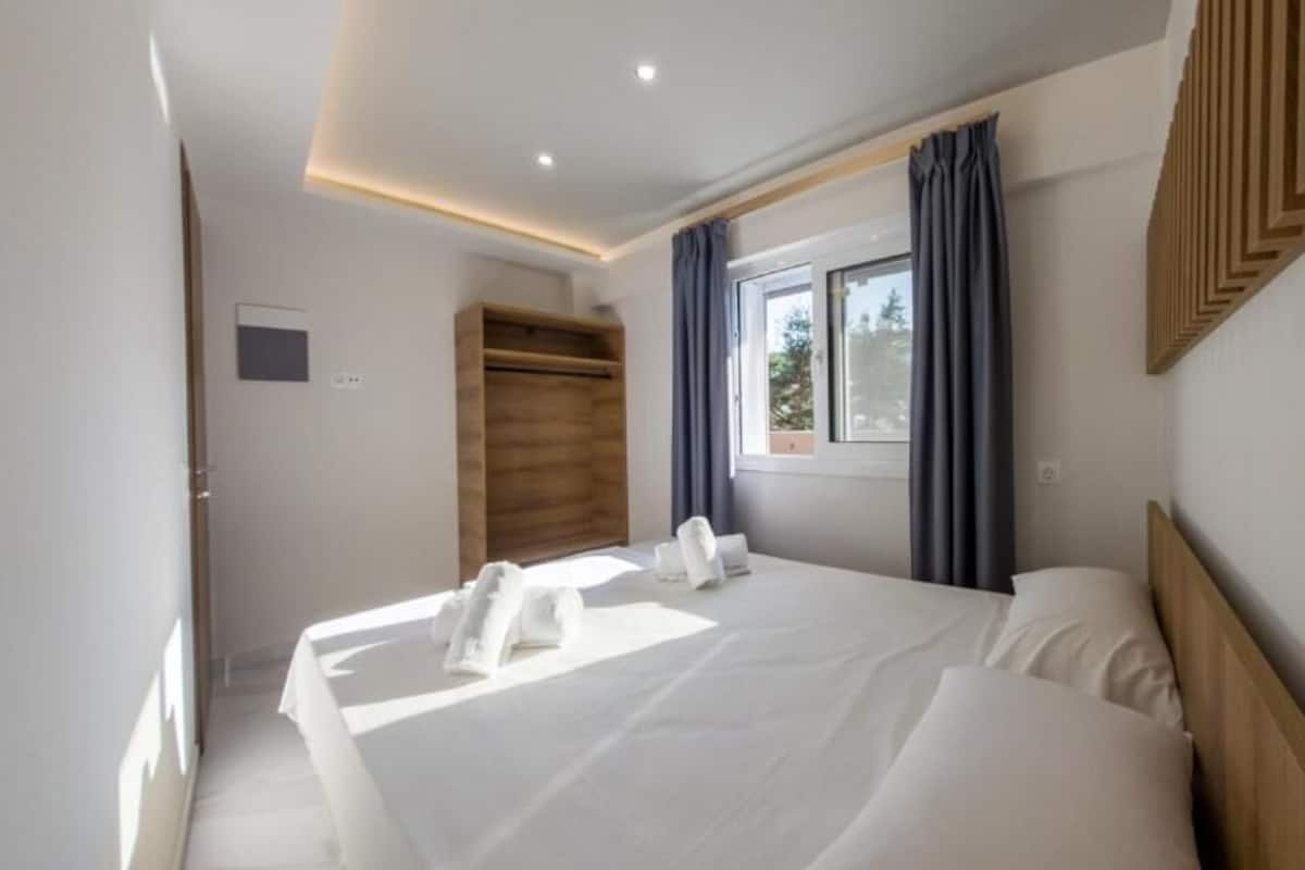Une chambre d’hôtel moderne dotée d’un grand lit, d’une tête de lit en bois, d’une fenêtre avec des rideaux et d’une armoire intégrée.