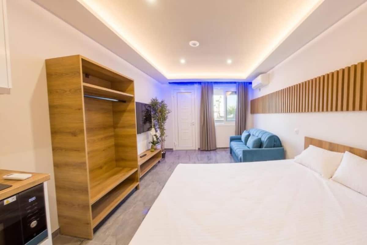 Une chambre d’hôtel moderne avec un grand lit, une armoire en bois, un coin salon avec un canapé bleu et une tête de lit en bois.