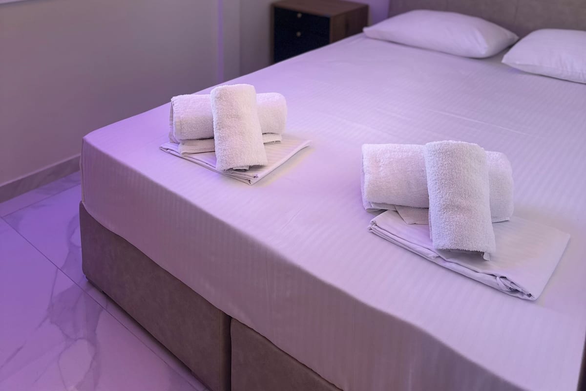 Une chambre d’hôtel avec un grand lit, deux serviettes enroulées, une table de chevet et une fenêtre donnant sur un paysage verdoyant.