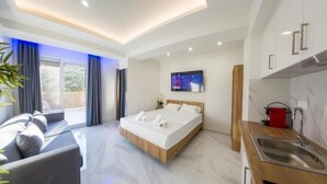 Una habitación de hotel moderna con cama, escritorio, televisor y zona de cocina.