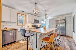 A modern kitchen with white cabinets, a central island with bar stools, stainless steel appliances, and pendant lighting. - 3BR Retreat: Peaceful, Mountain View, Pet Friendly (Boones Mill)