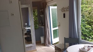 Une pièce comprenant une table à manger, des chaises, un petit coin cuisine et donnant sur un espace verdoyant.