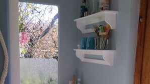 Une petite salle de bain avec une fenêtre, un lavabo blanc, un miroir et une étagère contenant des articles de toilette.