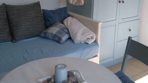 Une pièce avec un canapé bleu, une table blanche ornée d’une bougie et de quelques pierres, un meuble bleu et une chaise.