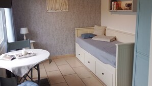 Une chambre à coucher comprenant un lit, une table de chevet, une chaise, une lampe, une étagère avec des livres et une horloge murale.