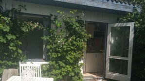 Une terrasse avec une table et des chaises blanches, une lanterne blanche et un arbuste vert.