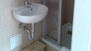 Une salle de bain avec un lavabo blanc, un miroir, un petit tabouret et un espace douche.