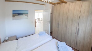 Een slaapkamer met twee bedden, een houten garderobe en een schilderij van een strandgezicht.
