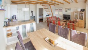 Een moderne keuken met houten balken, een eethoek met een houten tafel, en een woonkamer met een bank en televisie.