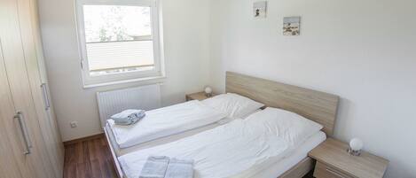 Un dormitorio con dos camas, piso de madera, una ventana y un radiador.