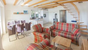 Een moderne woonkamer met een zithoek, een eethoek met stoelen, een keuken en een trap.