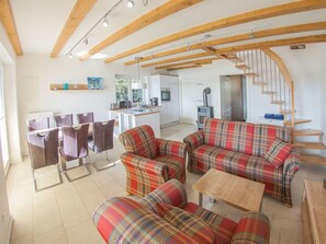 Ein modernes Wohnzimmer mit einer Sofagarnitur, einem Essbereich mit Stühlen, einer Küche und einer Treppe.