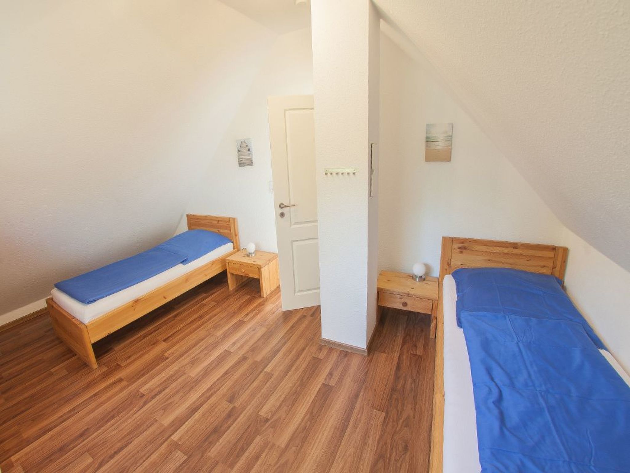 Una stanza piccola e pulita con due letti di legno, una porta bianca e un comodino con una lampada.