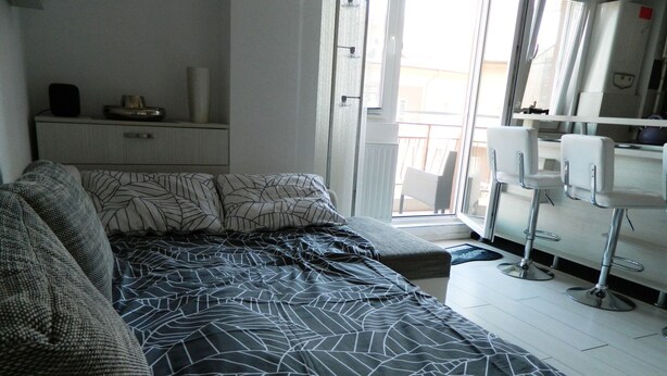 A modern bedroom with a large bed, a small seating area, a kitchenette, and a balcony with a view. - Wohnung "Militari Residence M1" by Interhome (Berceni)