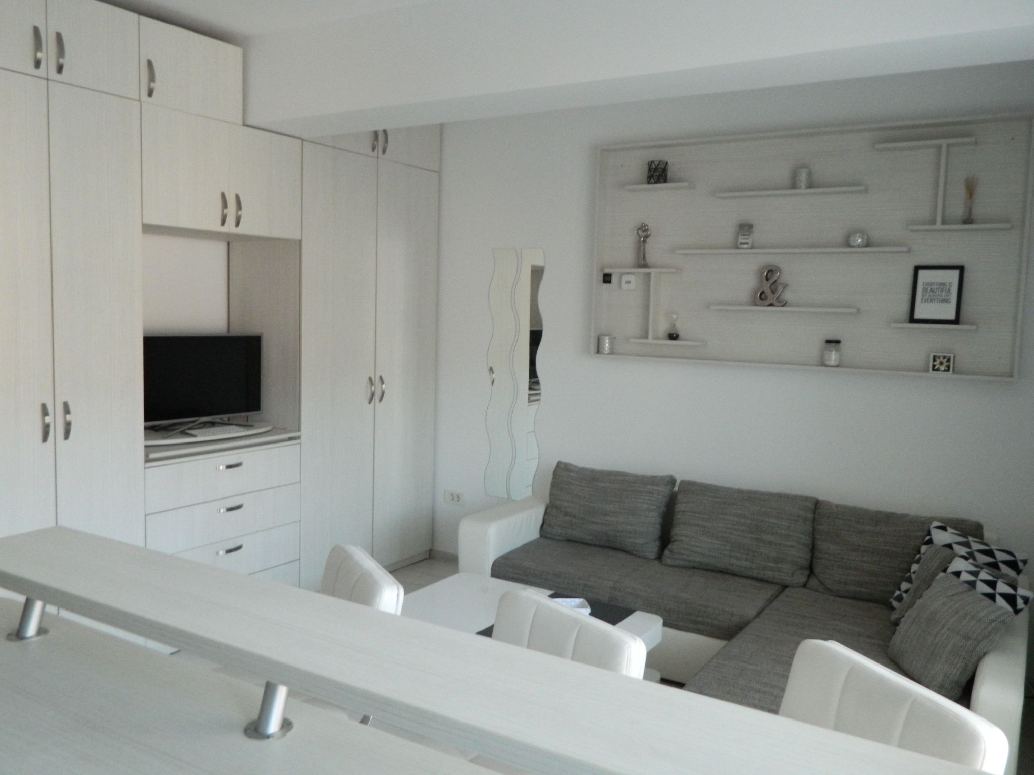 A modern living room with a grey sofa, white armchairs, a long white table, and built-in white cabinets.