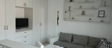 A modern living room with a grey sofa, white armchairs, a long white table, and built-in white cabinets.
