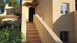 A building with a beige exterior, a tiled roof, and a staircase leading to a door. - Calarossa-Red Island First Row House with Sea View and Double Terrace (Trinità d'Agultu e Vignola)