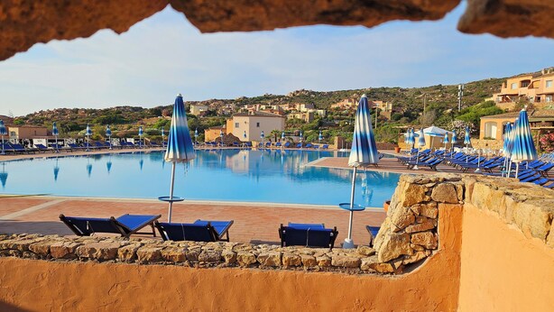 A pool area with lounge chairs and umbrellas, surrounded by stone walls and buildings in the background. - Calarossa-Red Island First Row House with Sea View and Double Terrace (Trinità d'Agultu e Vignola)