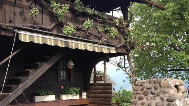 Un edificio rústico de madera con un porche cubierto, un muro de piedra y un banco de madera.