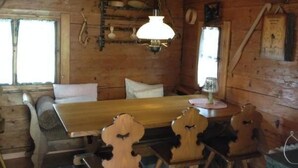 Interior de una cabaña de madera con una mesa de comedor, sillas, un banco y una lámpara colgante.