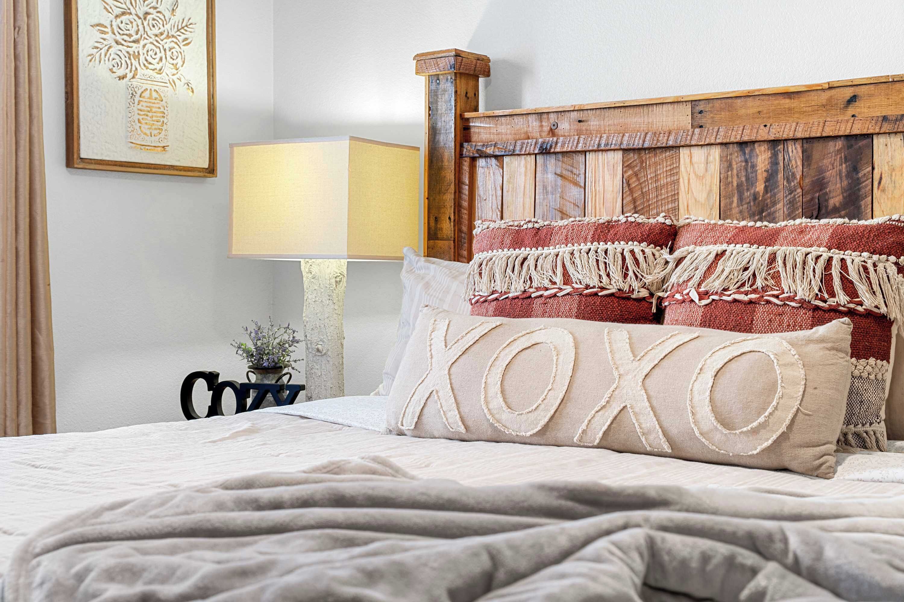 Ein ordentlich bezogenes Bett mit Holz-Kopfteil, einer Nachttischlampe und einem gerahmten Kunstwerk an der Wand.
