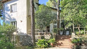 A two-story building with a stone facade, a tiled roof, and a paved entrance area with potted plants.