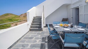 Un espace de repas extérieur moderne, avec une table dressée pour deux personnes, un escalier menant à un niveau supérieur et une vue sur le paysage.