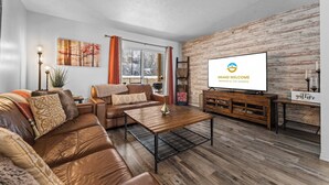 A modern living room with a leather sofa, a wooden coffee table, and a flat-screen TV on a wooden stand. - Ashley's Charming Chalet (Branson)