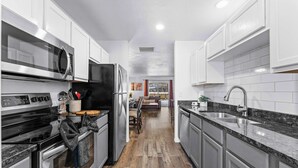 A modern kitchen with stainless steel appliances, white cabinetry, and a wooden floor. - Ashley's Charming Chalet (Branson)