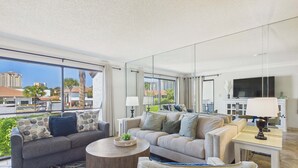 A modern living room with two sofas, a coffee table, and a TV. Large windows offer a view of the city. - Emerald's Edge 2306-Resort Living-Sleeps 8 (Panama City Beach)
