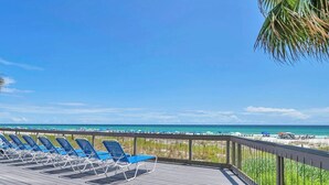 A wooden deck with blue lounge chairs facing a beach. - Emerald's Edge 2306-Resort Living-Sleeps 8 (Panama City Beach)