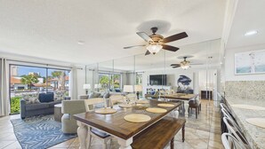 A spacious living area with a dining table, sofas, and a ceiling fan. - Emerald's Edge 2306-Resort Living-Sleeps 8 (Panama City Beach)