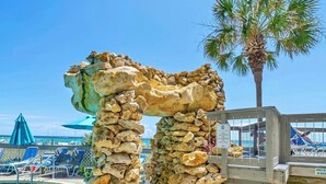 A stone archway at a poolside area with a sign prohibiting climbing or touching the rocks. - Emerald's Edge 2306-Resort Living-Sleeps 8 (Panama City Beach)