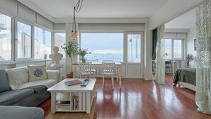 Un ampio soggiorno con una grande finestra che offre una vista panoramica, un'area pranzo con mobili bianchi e un angolo salotto accogliente con un divano grigio e un tavolino da caffè bianco.