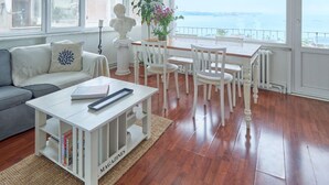Un soggiorno spazioso con vista sul mare, un divano bianco, un tavolo da pranzo con sedie e una libreria.