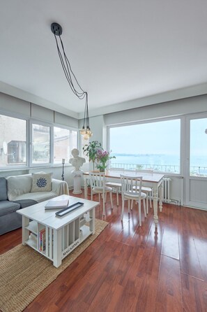 A spacious living room with a view of the sea, a white sofa, a dining table with chairs, and a bookshelf. - Wohnung mit Blick auf die Halbinsel von Istanbul by Interhome (Istanbul)
