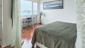 Una camera da letto con un letto, una scrivania con sedie, una ventola e una finestra vista sulla città.