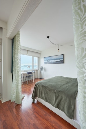 A bedroom with a bed, a desk with chairs, a fan, and a window with a view of a cityscape. - Wohnung mit Blick auf die Halbinsel von Istanbul by Interhome (Istanbul)