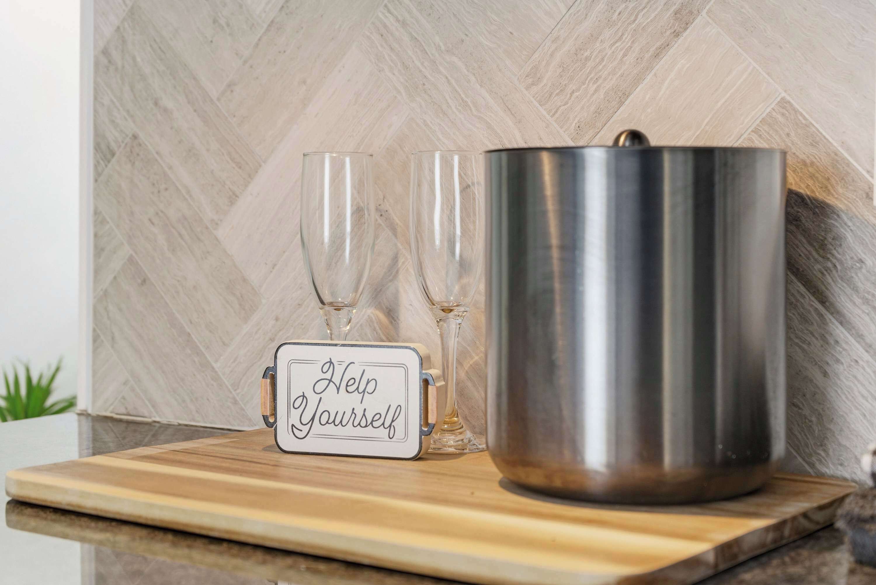 Un comptoir de cuisine avec une casserole en acier inoxydable, deux verres à vin et un panneau indiquant : « Servez-vous. »