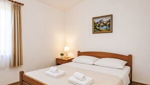 Habitación de hotel con cama de madera, una mesita de noche con lámpara, un cuadro en la pared y una ventana con cortinas.