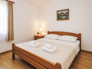 A hotel room with a wooden bed, a nightstand with a lamp, a painting on the wall, and a window with curtains. - Ein Apartment im Ferienhaus Zweirosen by Interhome (Fažana)