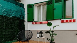 En uteplats med en stol, ett litet bord med en flaska och glas, och en krukväxt.