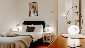 Ett sovrum med en säng, sänglampor, ett sängbord, en spegel och en dörr.