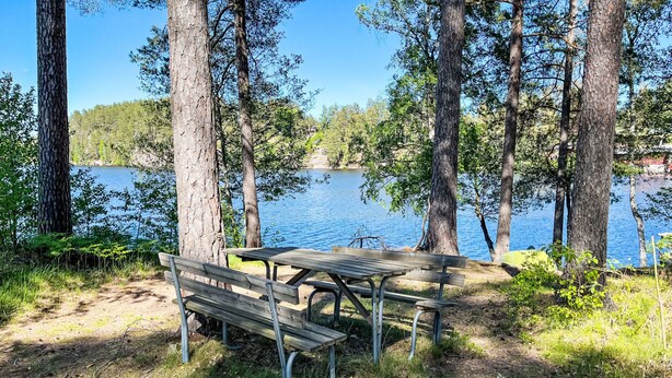 A picnic table and bench by a lake surrounded by trees. - Villa Daniel by Interhome (Storebro)