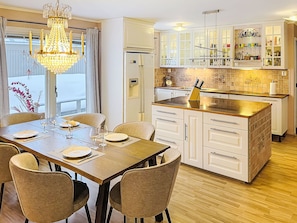 A modern kitchen with white cabinetry, a central island, and a dining area with a chandelier. - Villa Daniel by Interhome (Storebro)