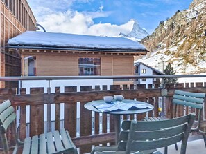 Een houten chalet met balkon, een tafel met stoelen en uitzicht op de bergen.