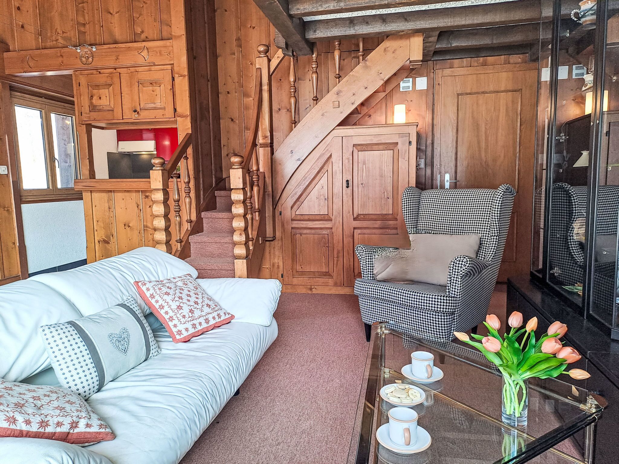 Ein gemütlicher Raum mit einer Holztreppe, einem Hundeprozess-Sessel, einem weißen Sofa und einem Glastisch mit einer Tulpenvase.